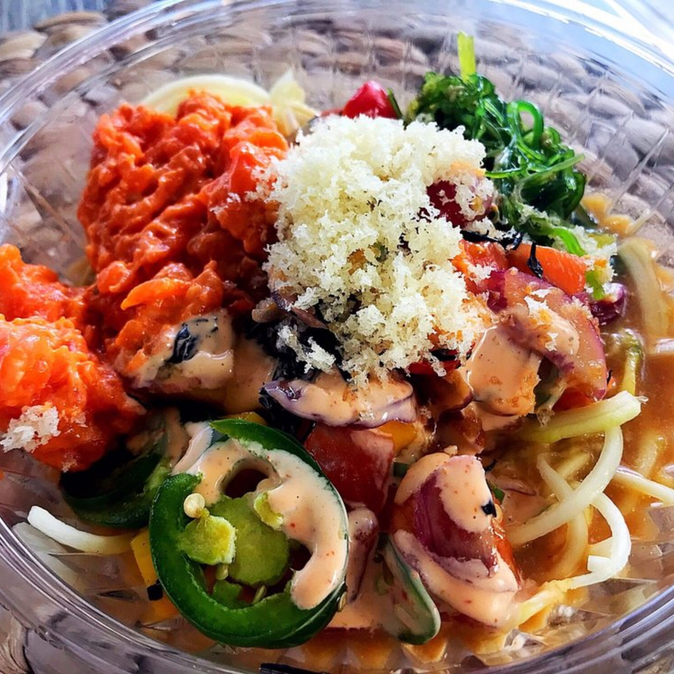 Close-up of a colorful Poke Ice poke bowl with various toppings in a clear container.